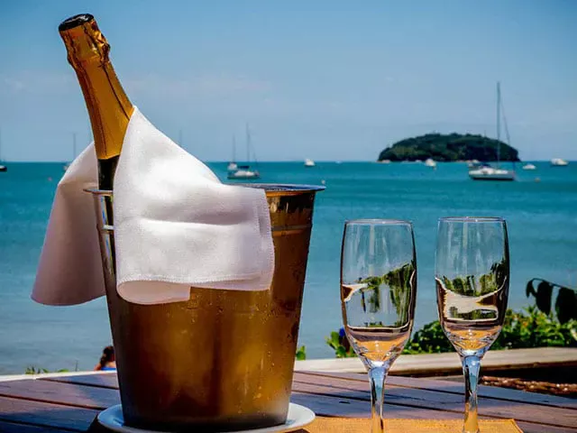 Balde com champagne e dois copos sobre mesa em deck frente mar na praia de Jurerê em Florianópolis, servidos no Restaurante Alameda dos Sabores